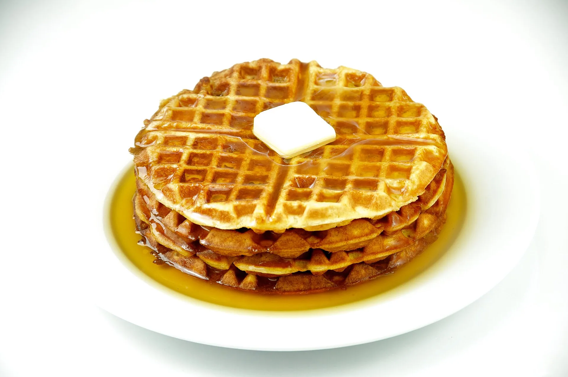 Stack of waffles topped with butter in a pool of syrup on a plate