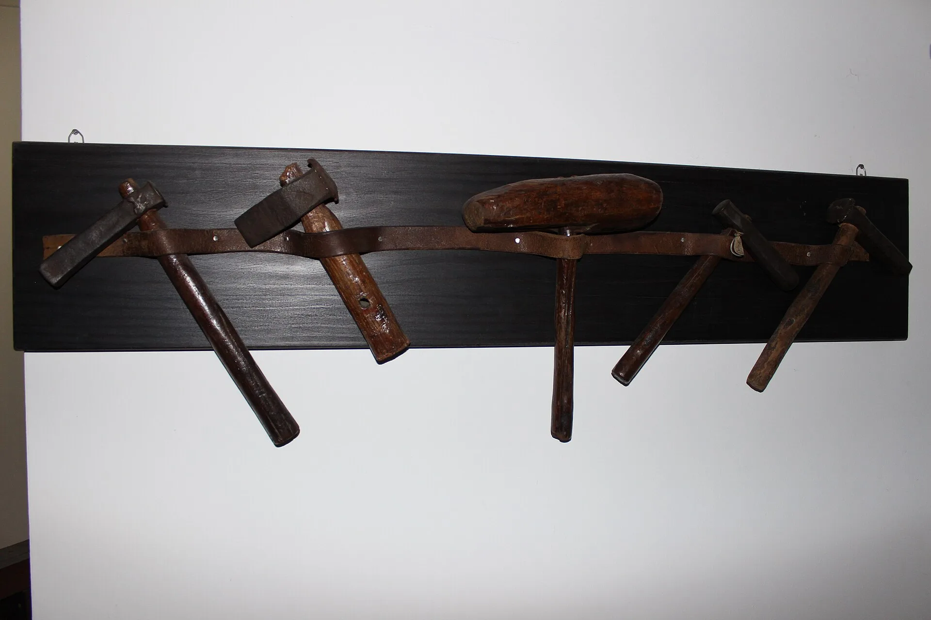 Row of old metalworking hammers hanging on a dark wooden wall rack