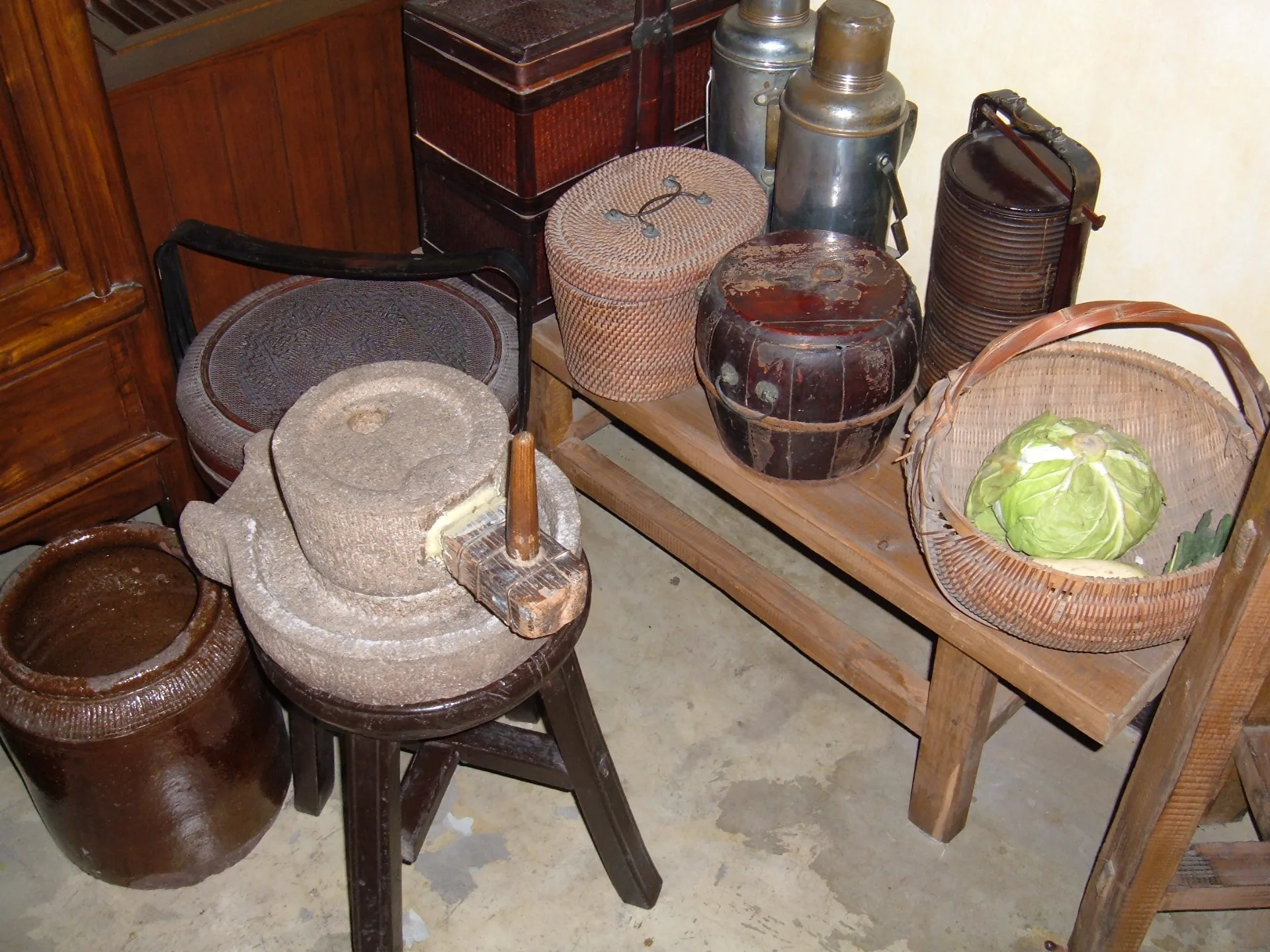 Stone hand mill, baskets, jars and flasks on wooden stools in a kitchen