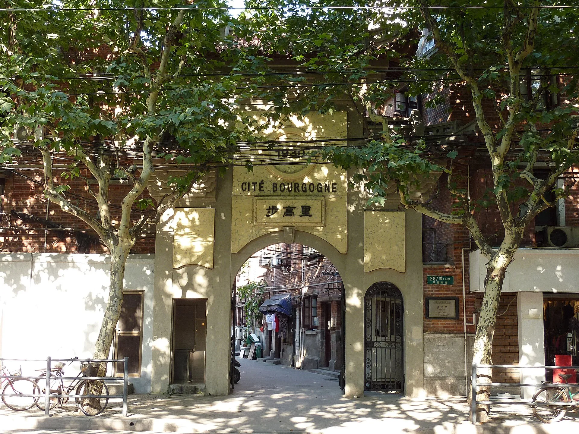 Arched entrance gate to a lane flanked by plane trees and parked bicycles