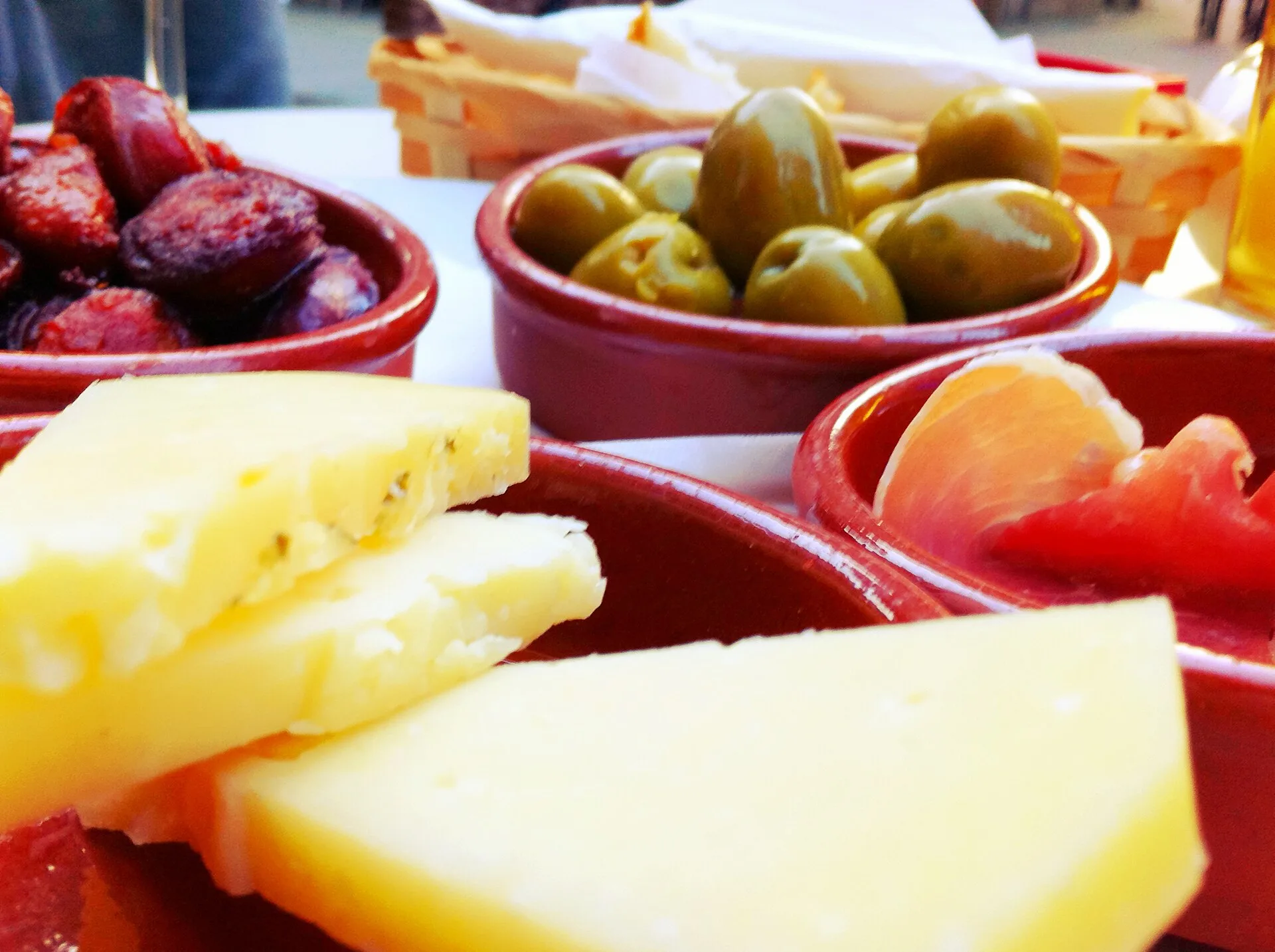 Small bowls of olives and cured meat beside slices of cheese