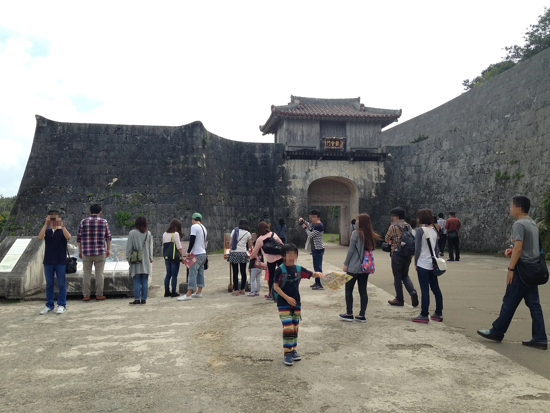 Visitors walking towards an arched stone gate in curved limestone walls
