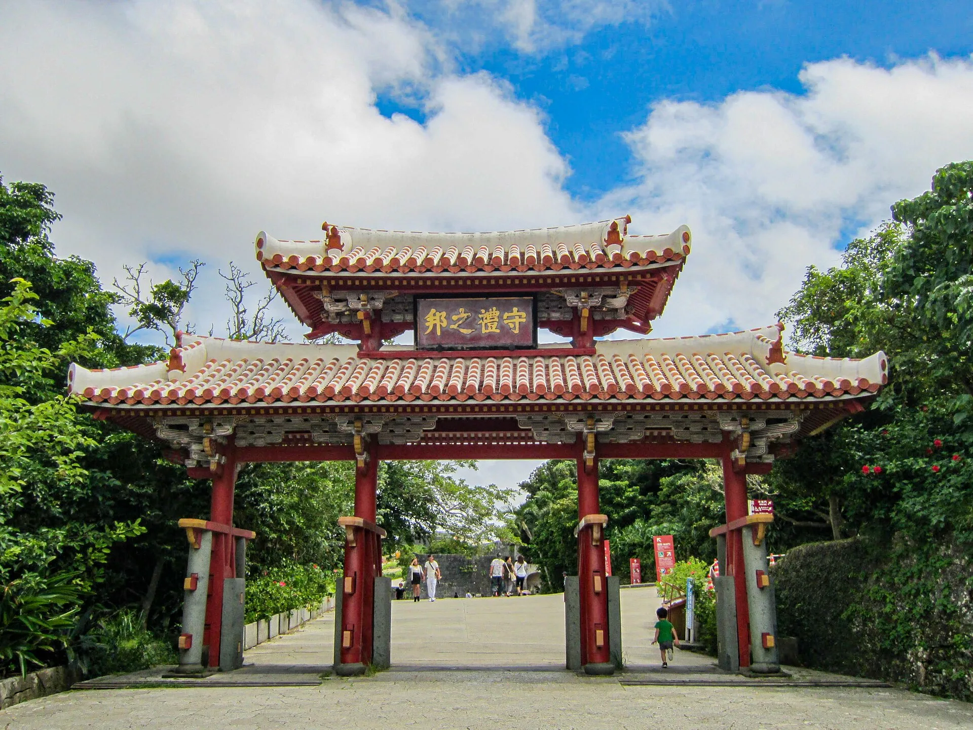 Red timber gate with two tiled roofs and a plaque, framed by trees