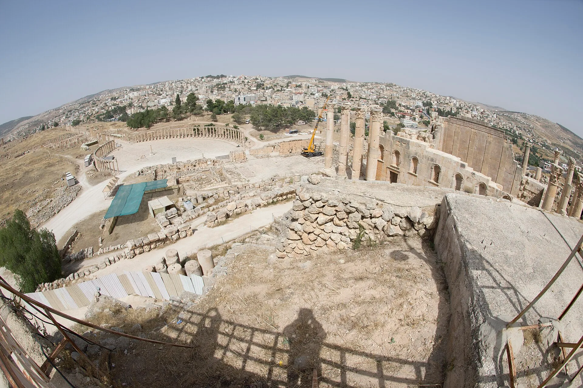 Wide view over a Roman theatre stage and seating towards ruins and a town