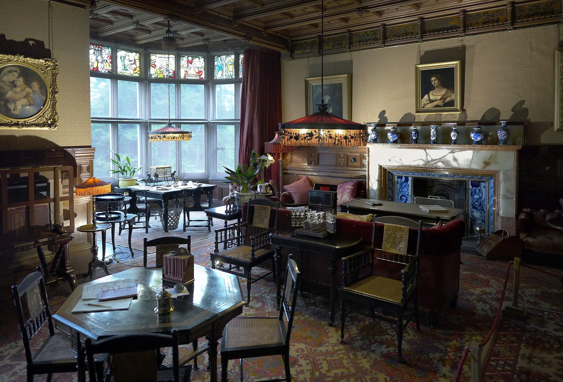 Panelled library with bay windows, tables, chairs and a tiled fireplace