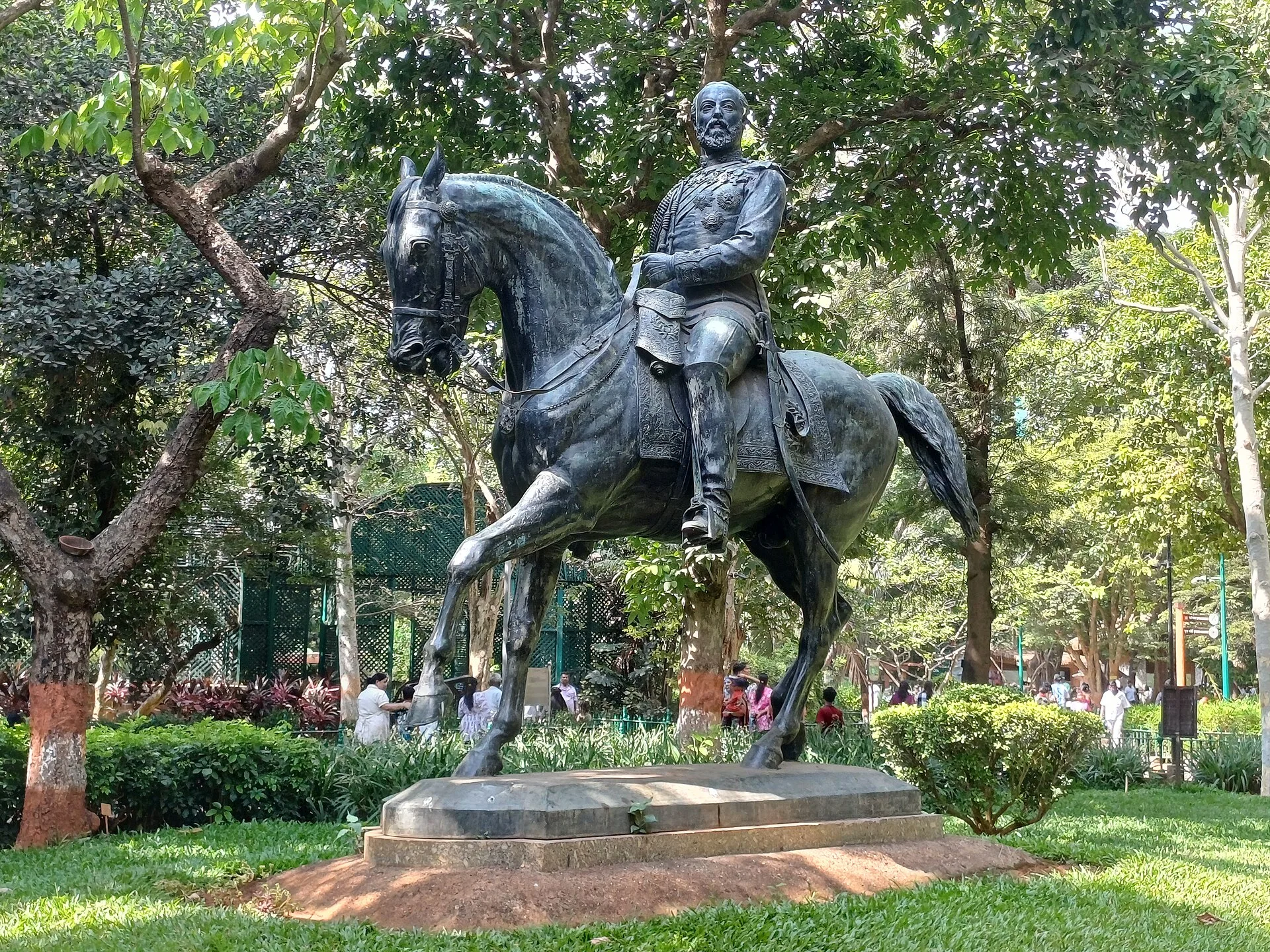 Dark bronze statue of a rider on horseback on a plinth among garden trees