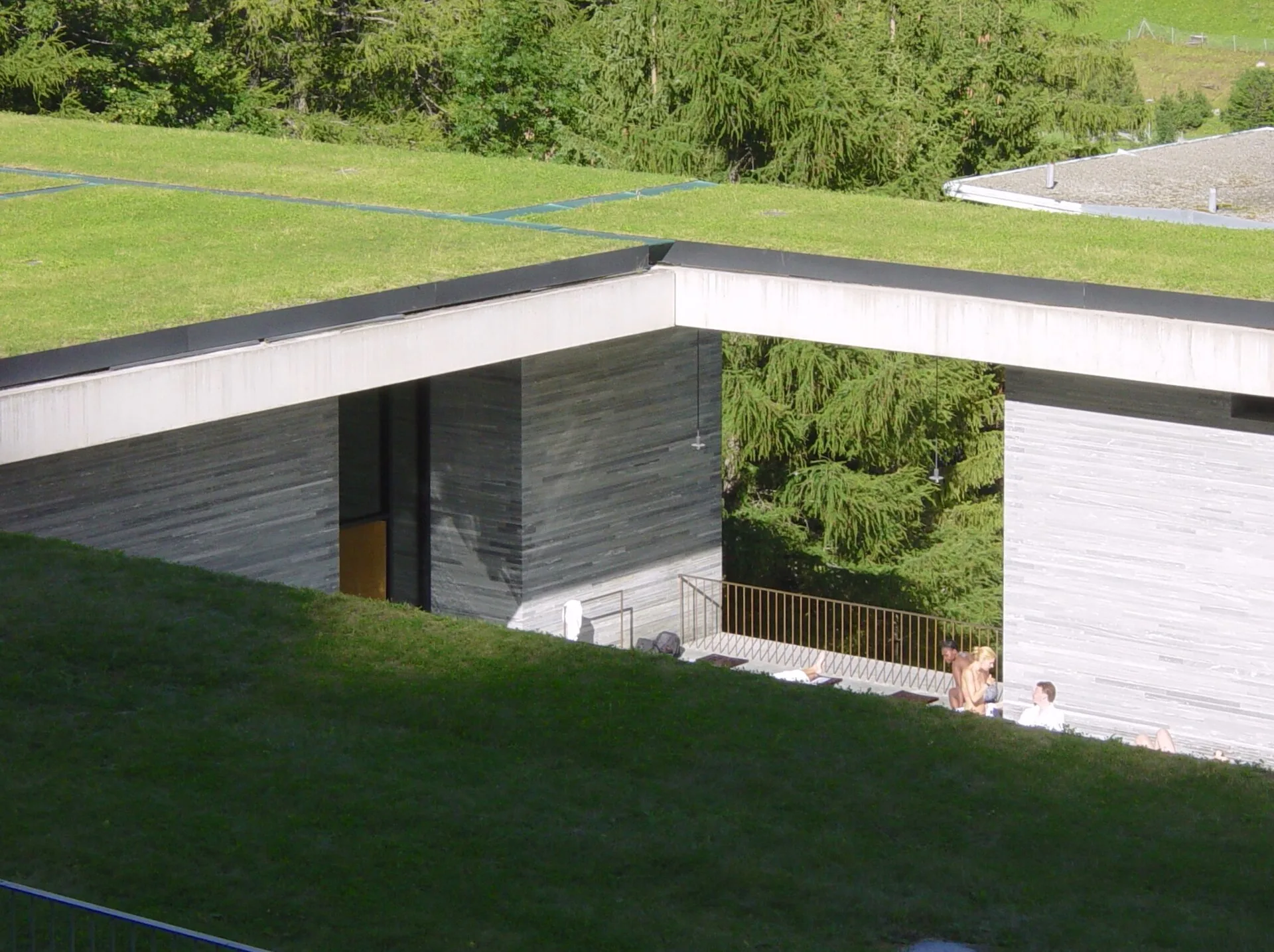 Grass-covered flat roof edge above a stone building opening onto a terrace