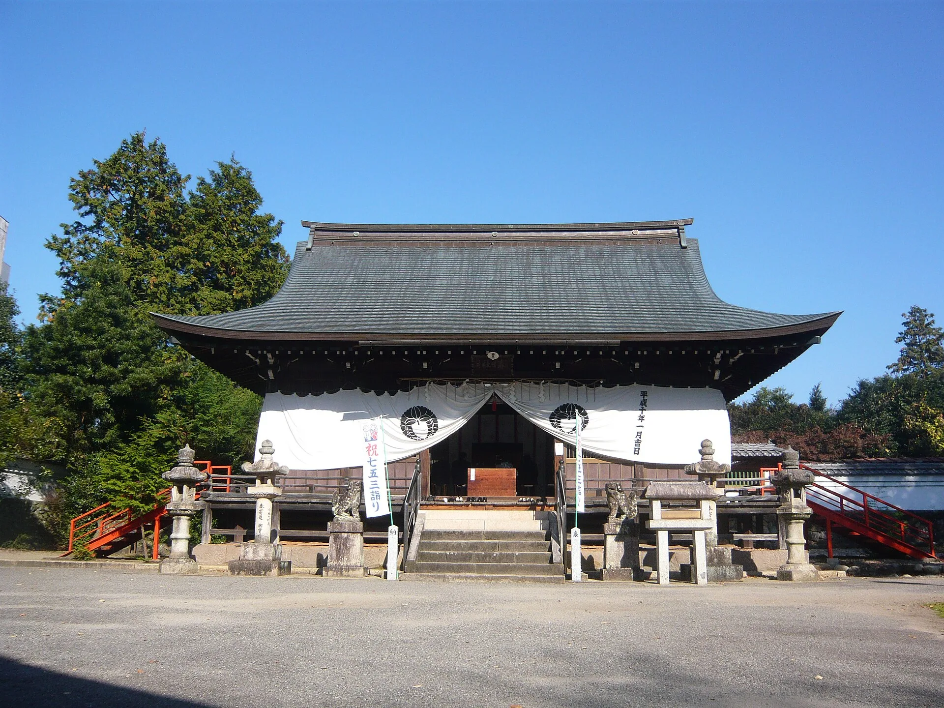 Wooden shrine hall with a dark tiled roof and stone lanterns in front