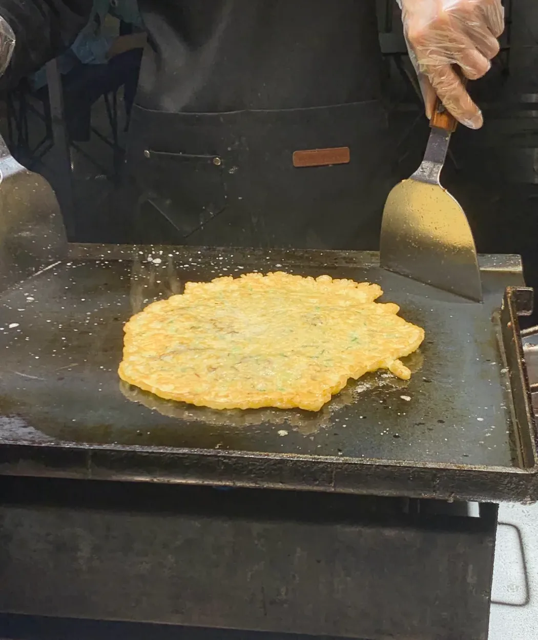 Cook in gloves turning a golden oyster omelette on a flat griddle with a spatula