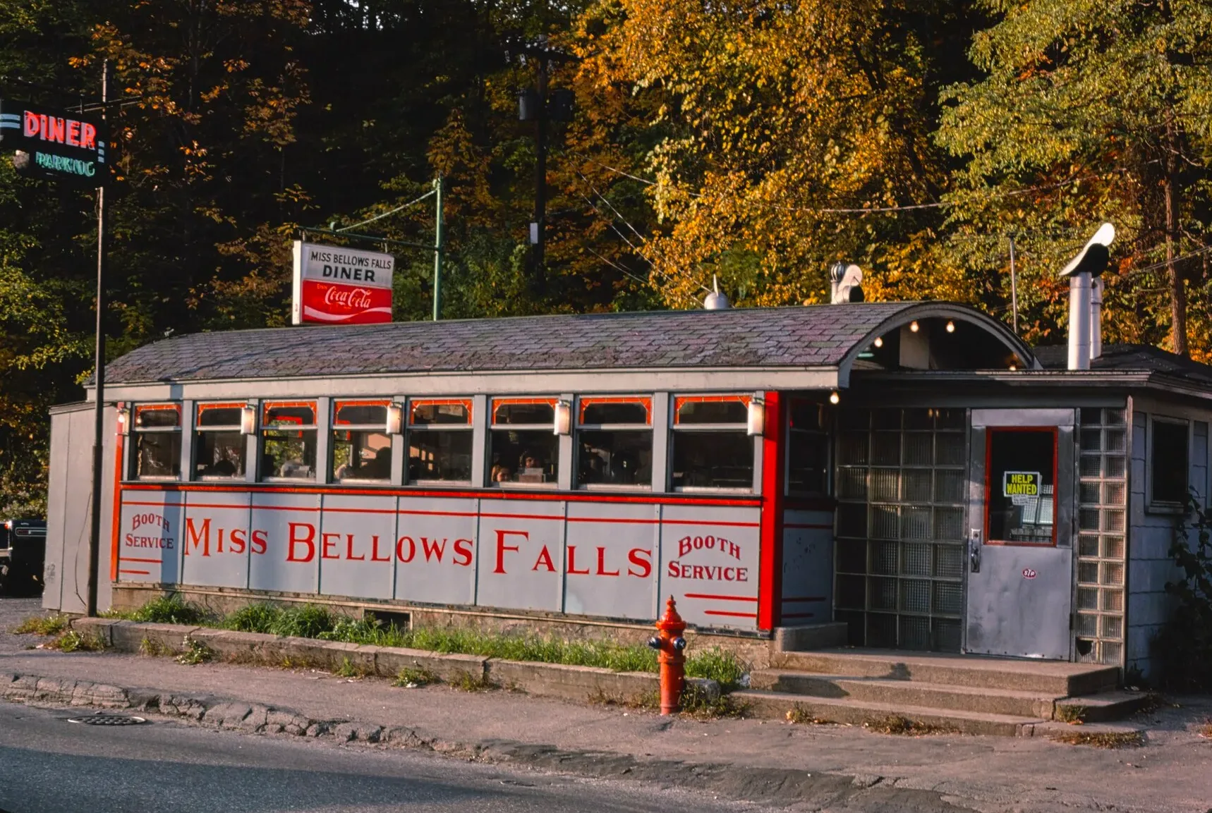 Red and white lunch car diner beside a road with autumn trees behind