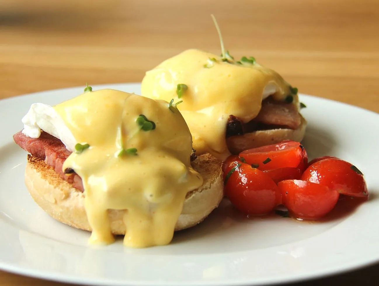 Two poached eggs with hollandaise on muffins beside cherry tomatoes on a plate