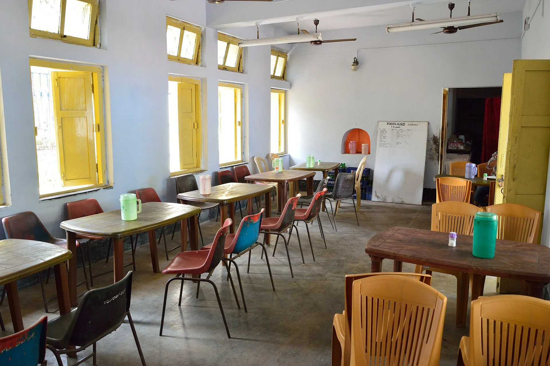 Empty canteen with hard floor, plastic chairs, tables and tall yellow-framed windows