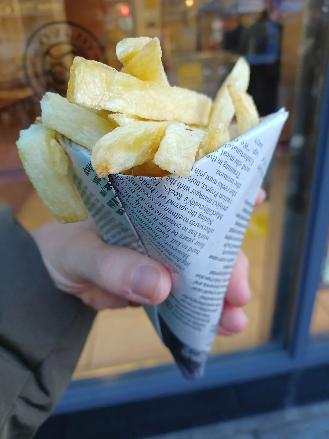 Hand holding a cone of newspaper filled with thick-cut chips