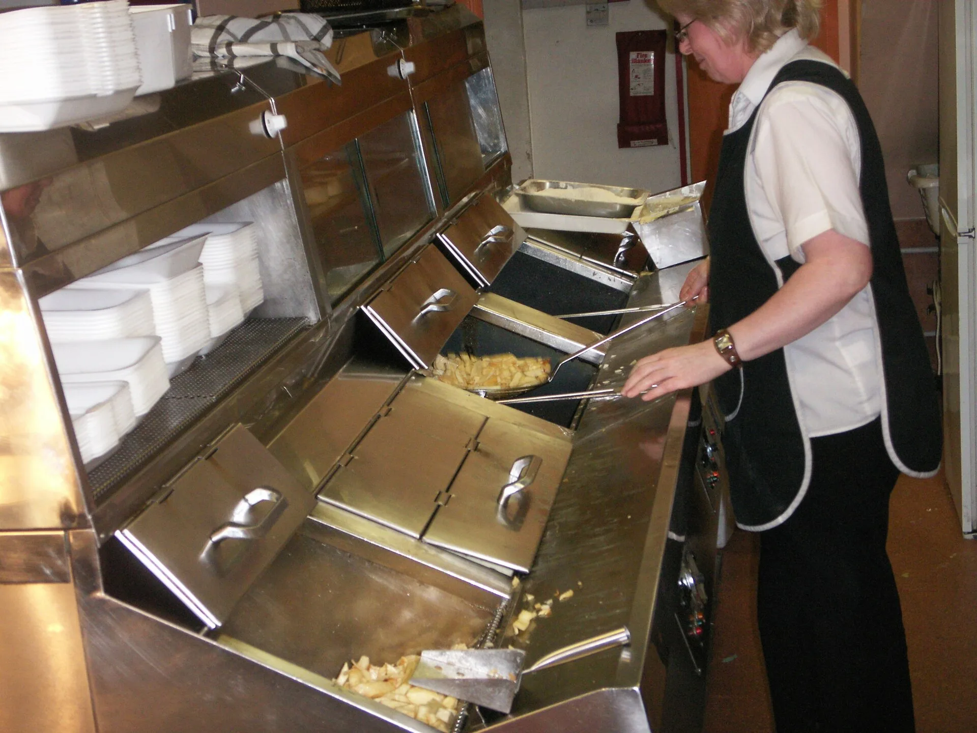 Stainless steel frying range with fryers and a worker in an apron