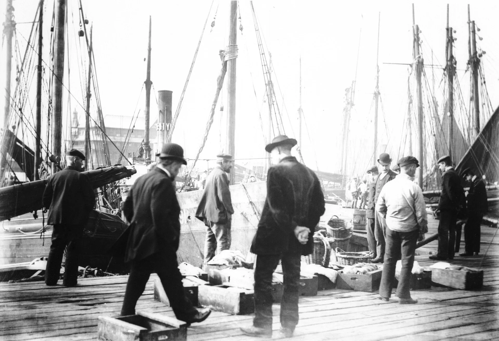 Black and white quayside with fishermen, baskets and masts of fishing boats