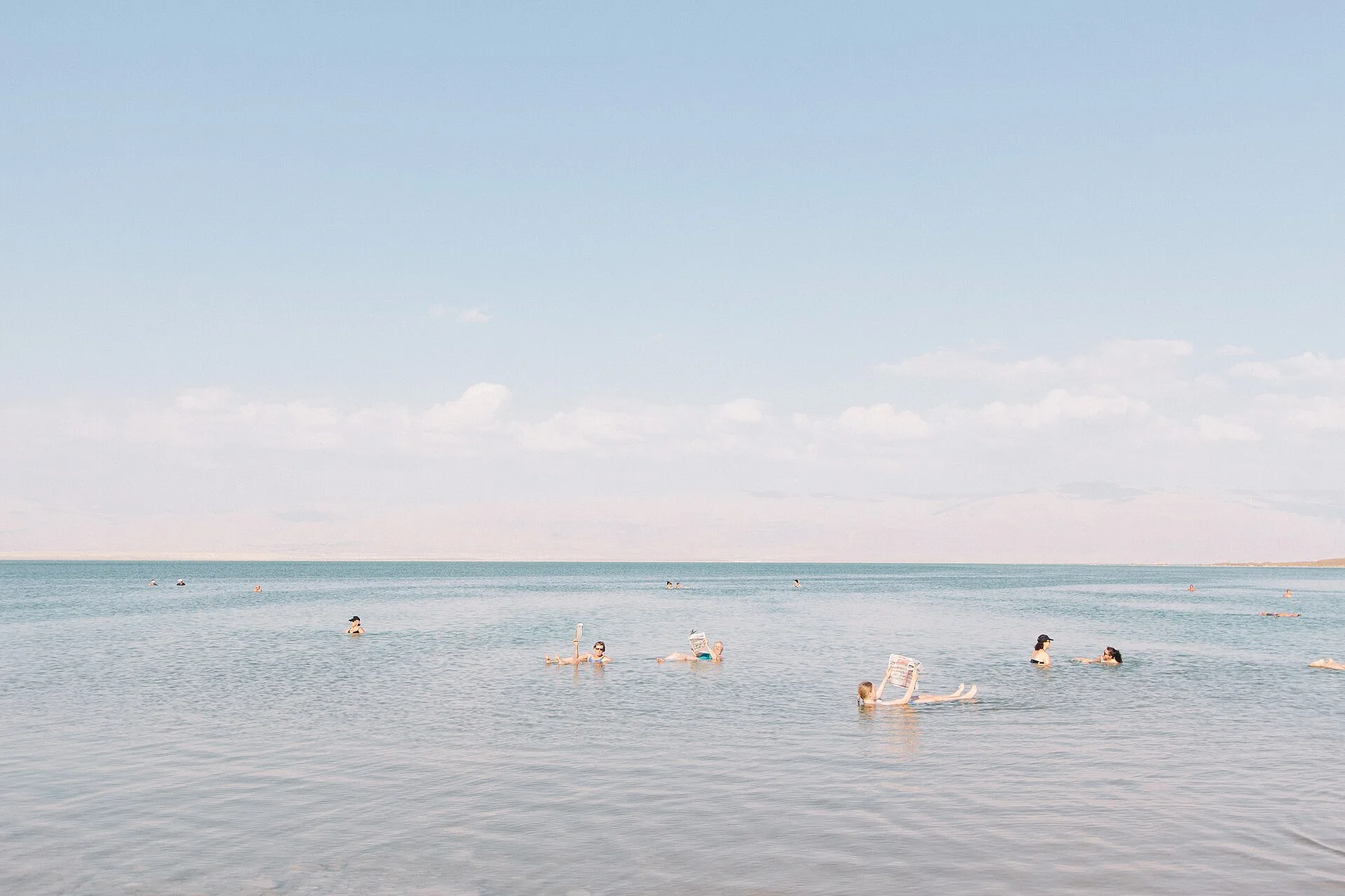 Several people floating in calm, pale water under a hazy sky