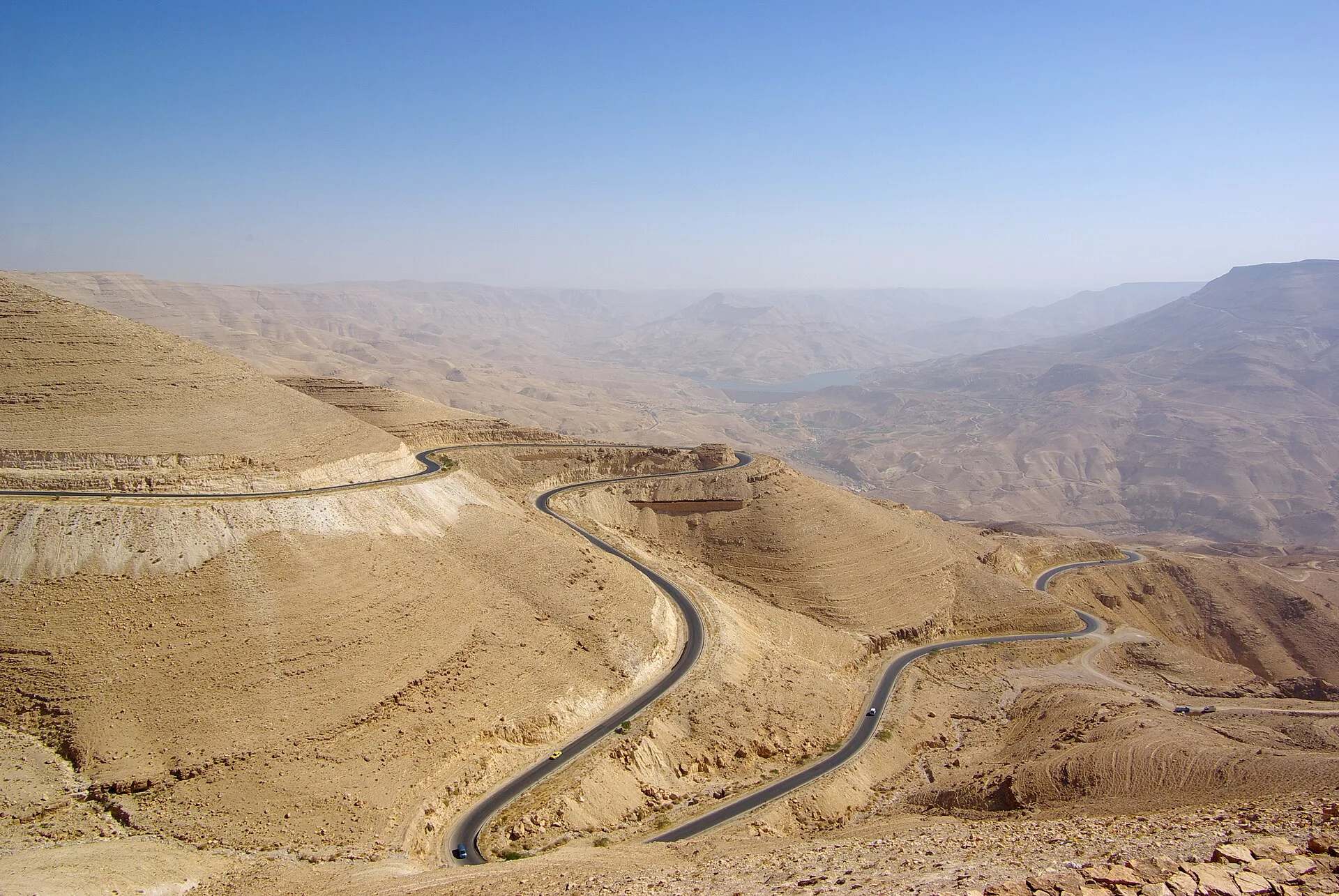 Winding road crossing dry, folded desert hills under a hazy sky