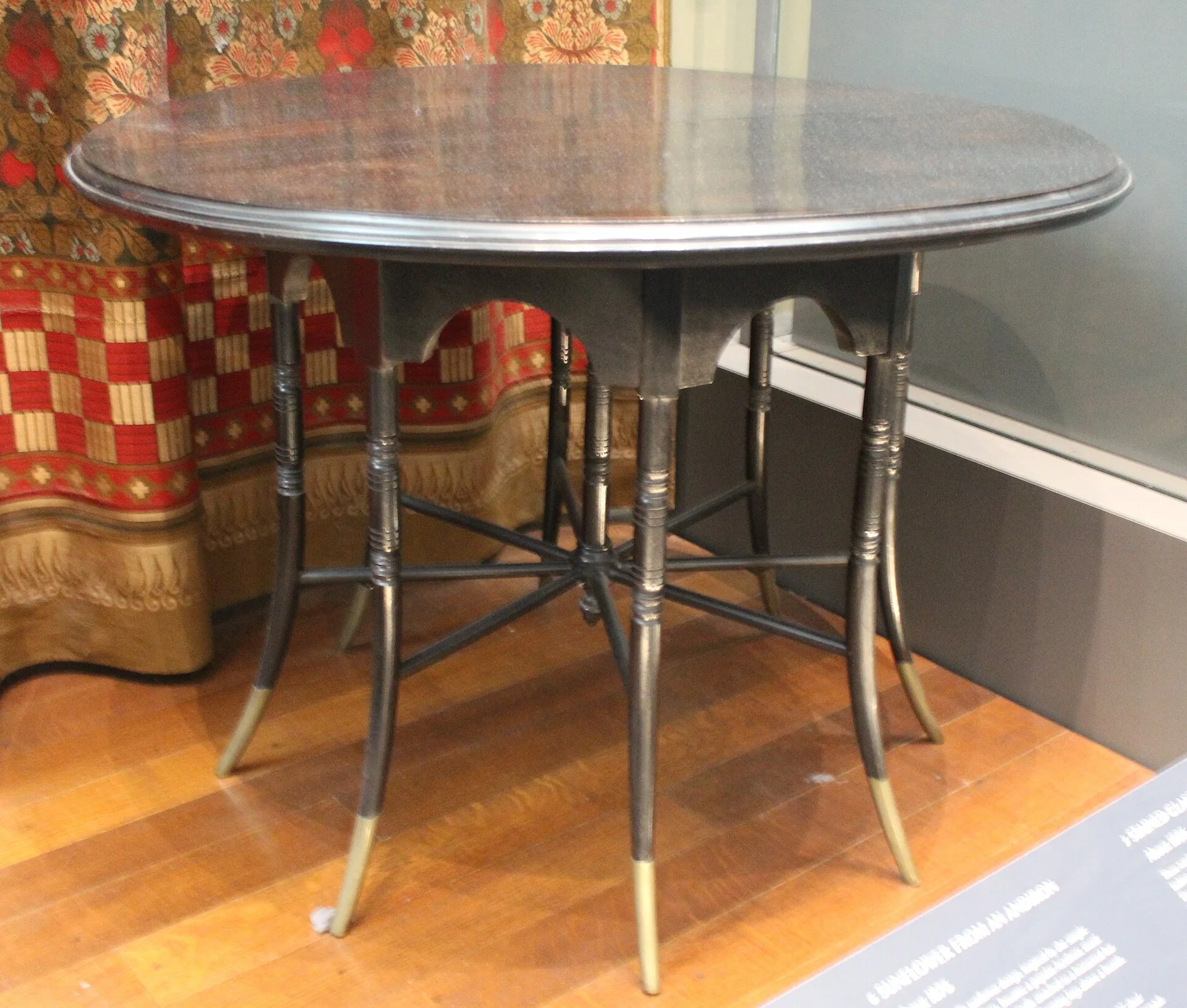Round black wooden table with slender legs and brass feet