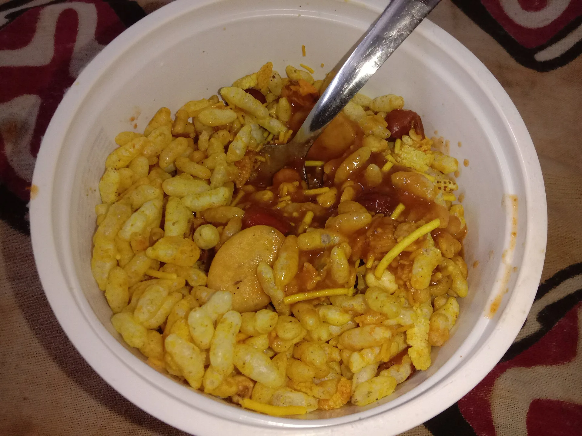 Bowl of puffed rice snack with sev and sauce and a spoon