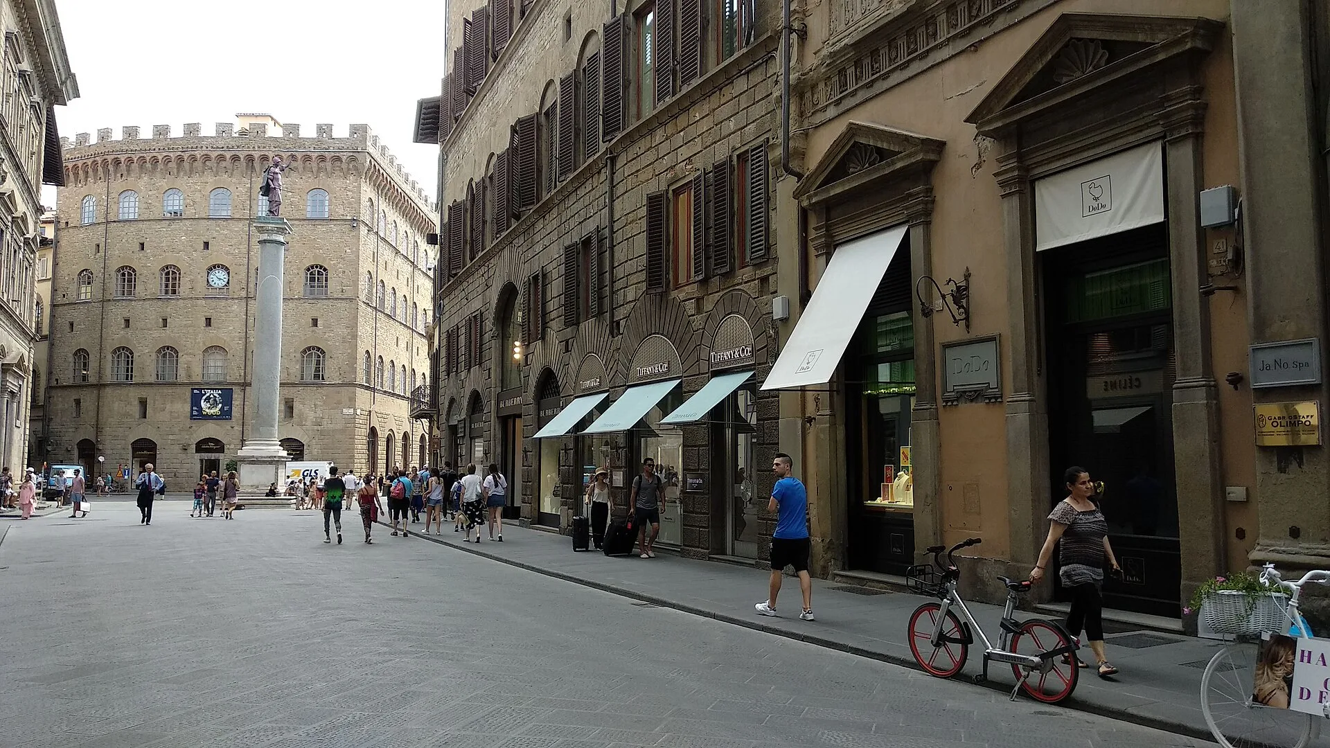 Stone palazzo street with shop awnings leading to a square with a column