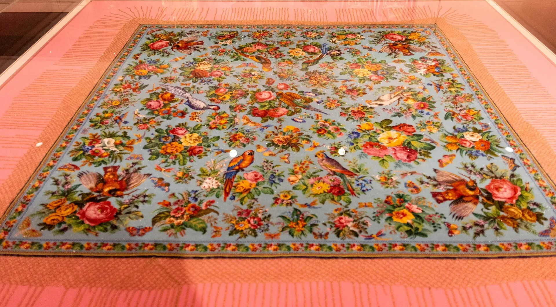 Beaded textile covered in colourful flowers and birds on a pale blue ground