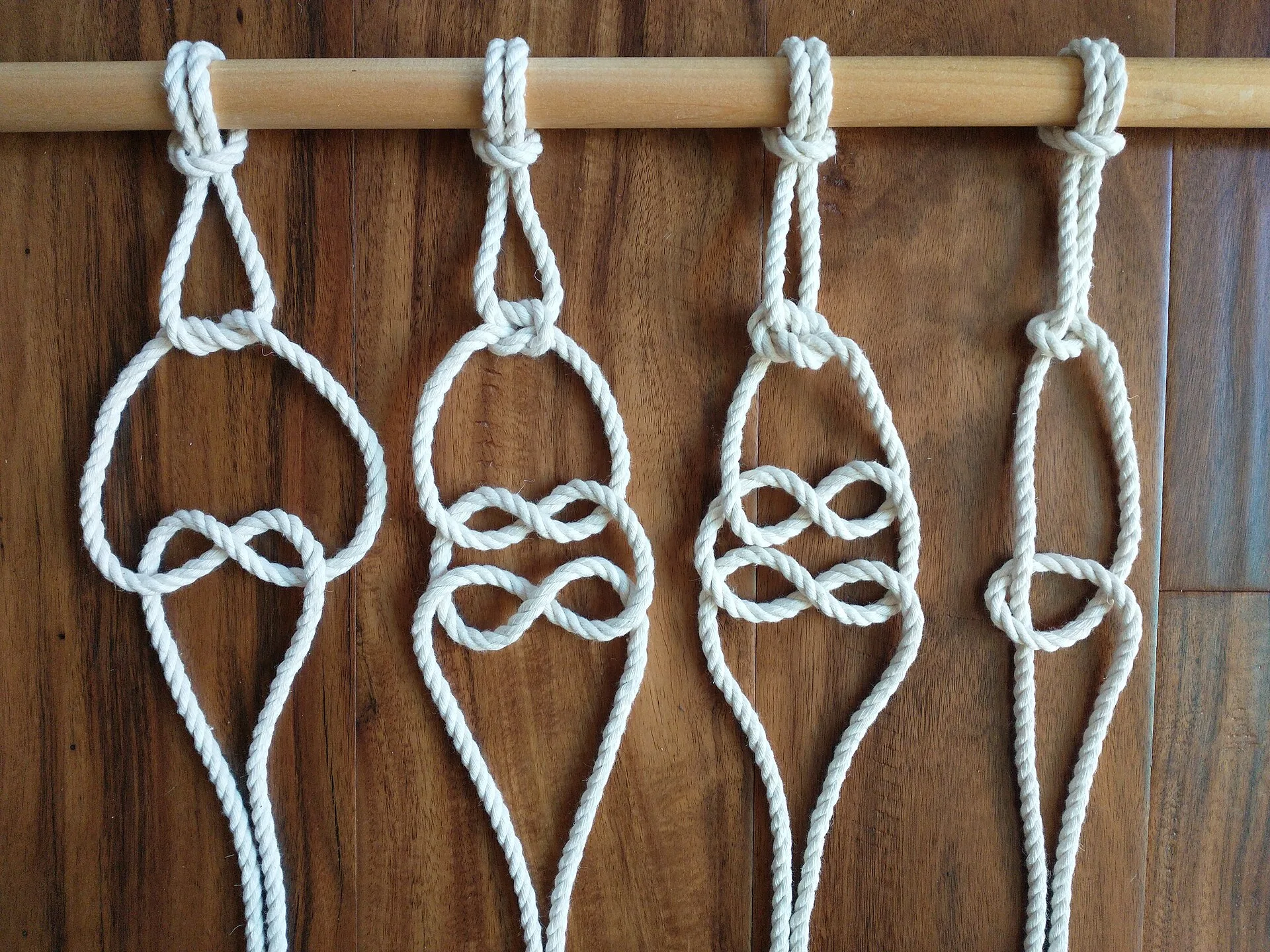 Four white cord samples showing different knots hanging from a wooden rod