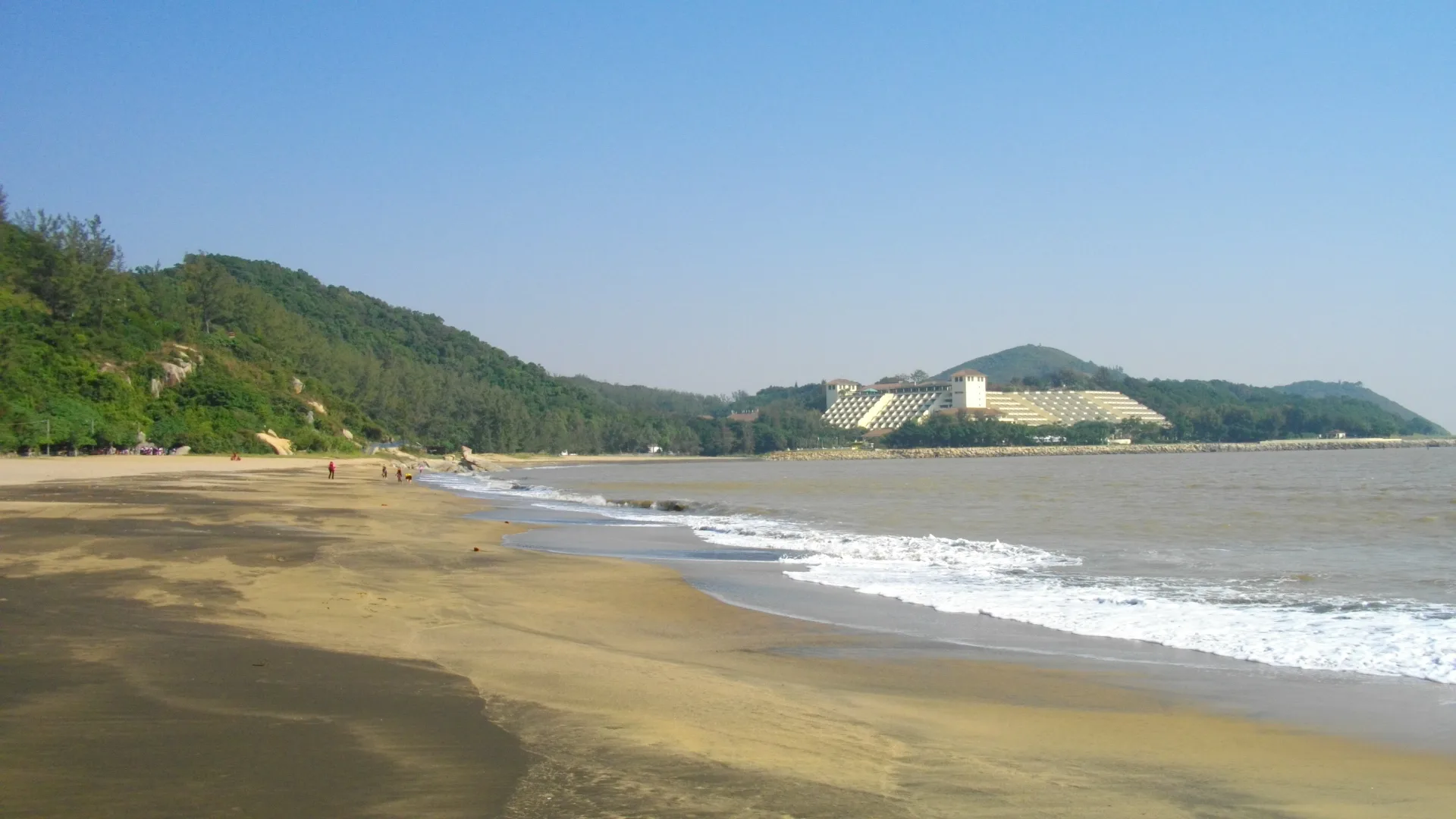 Sandy beach curving toward green hills with waves breaking on the shore