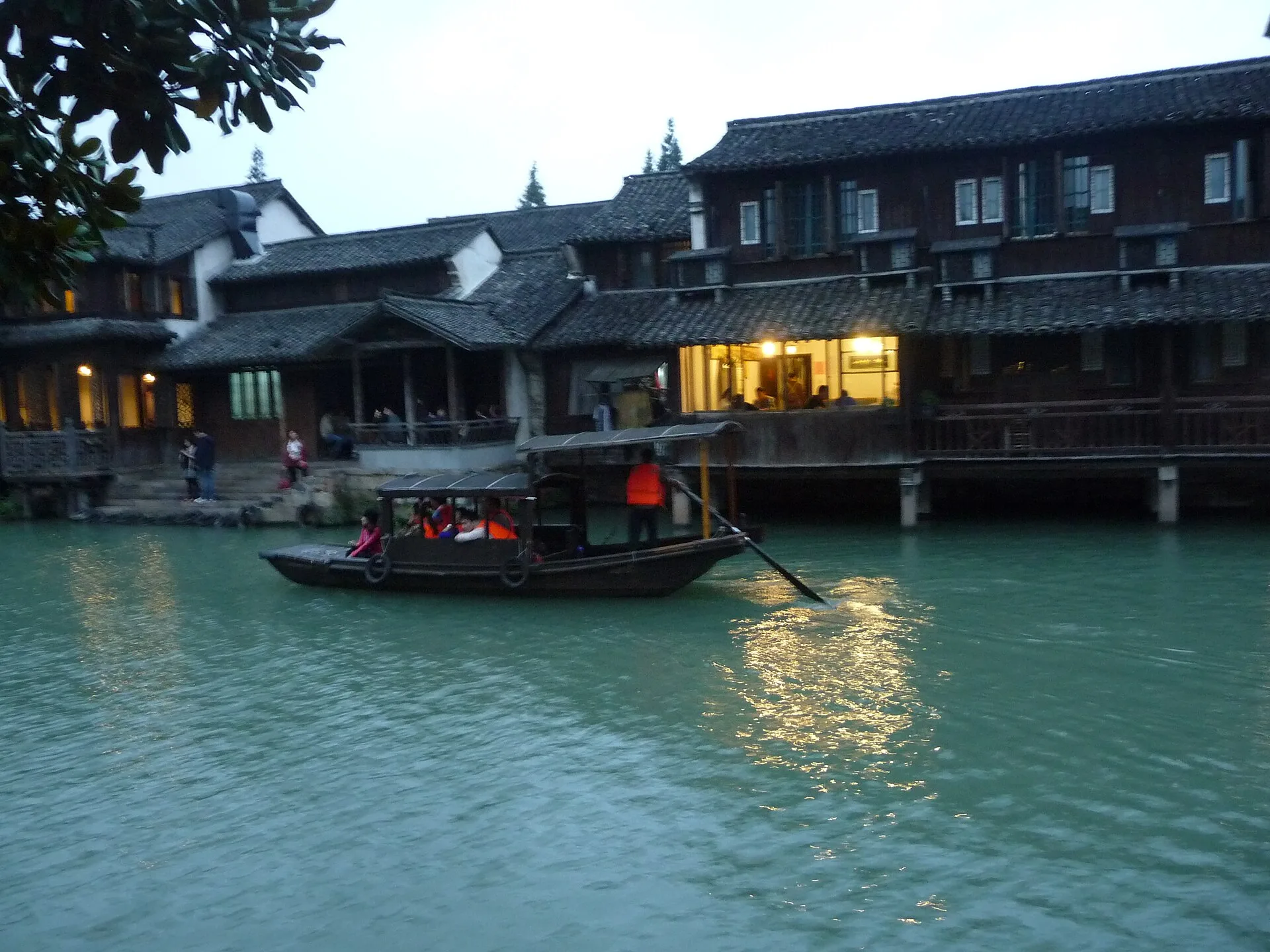 Boat passing two-storey wooden houses along a turquoise canal