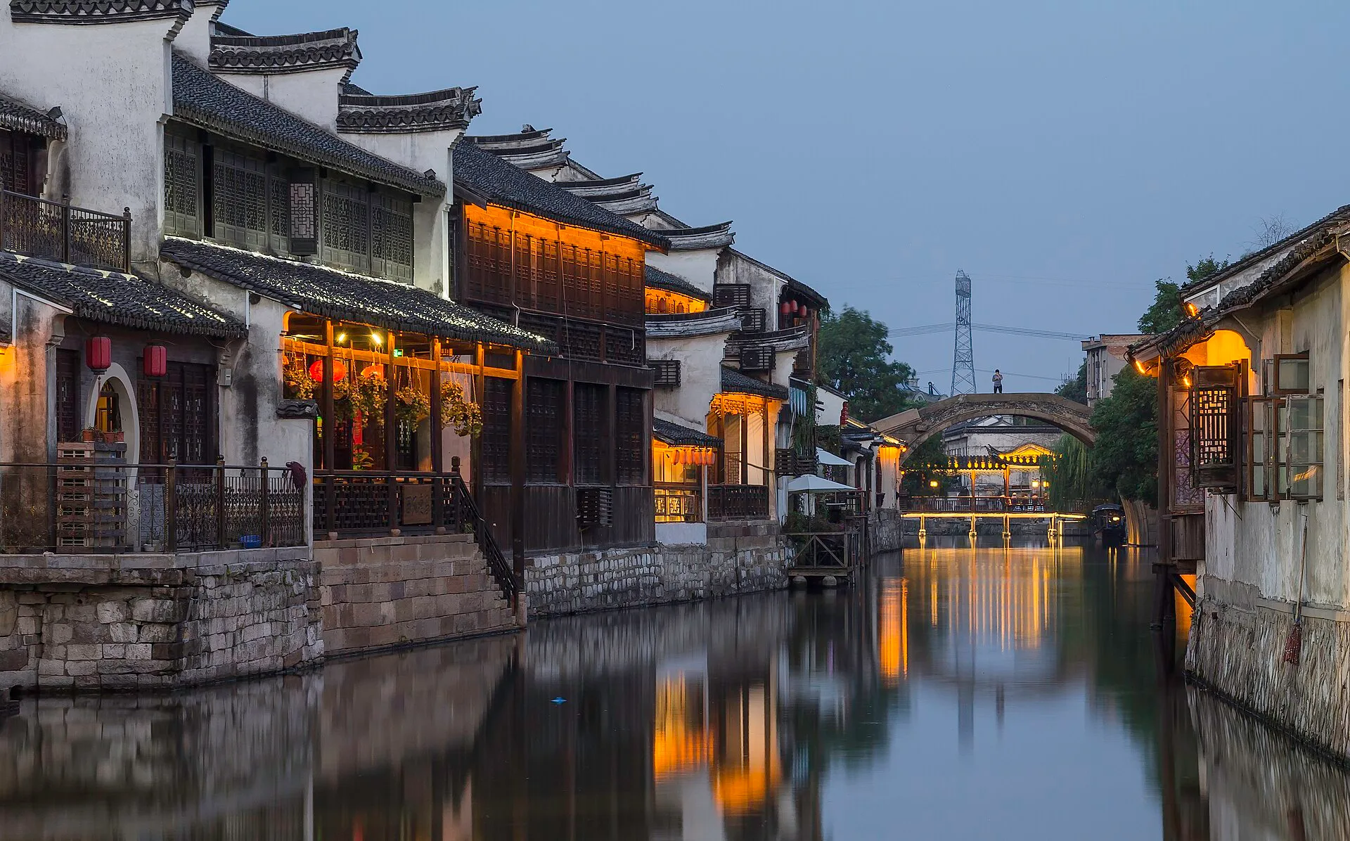 Lit shopfronts and houses reflected in a canal at dusk