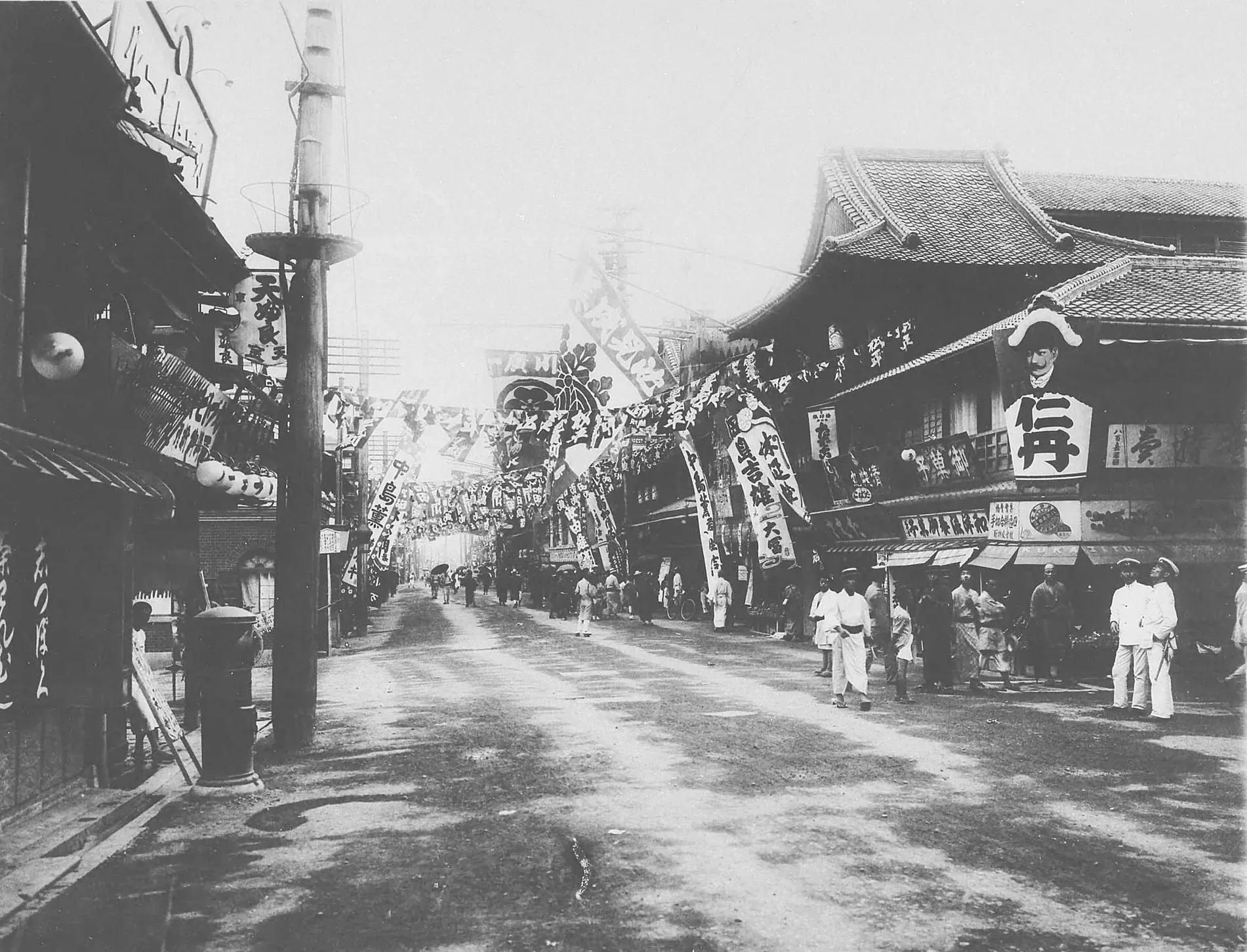 Black and white street view with theatre banners, wooden buildings and pedestrians