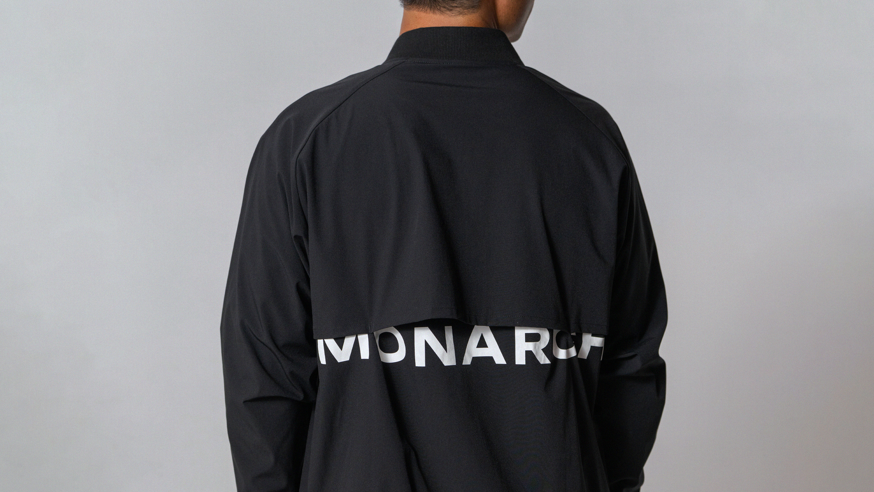 Person wearing a black jacket with white text partially visible on the back reading 'MONARCH'.