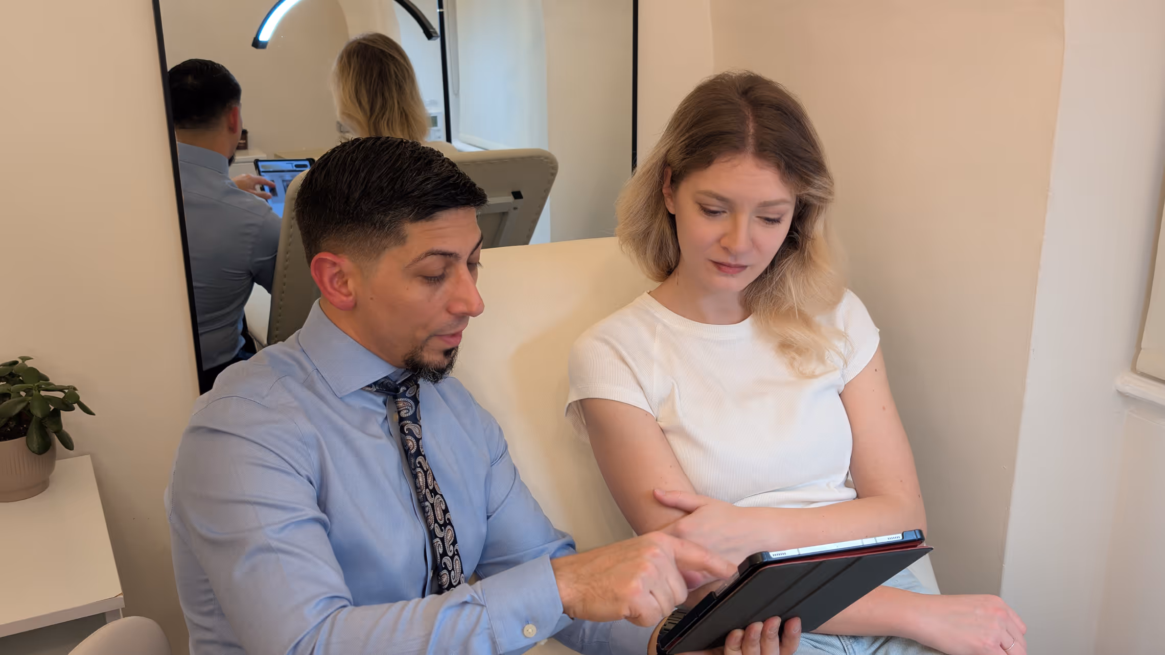 A man and woman sitting together in a chair, both focused on a tablet in their hands.