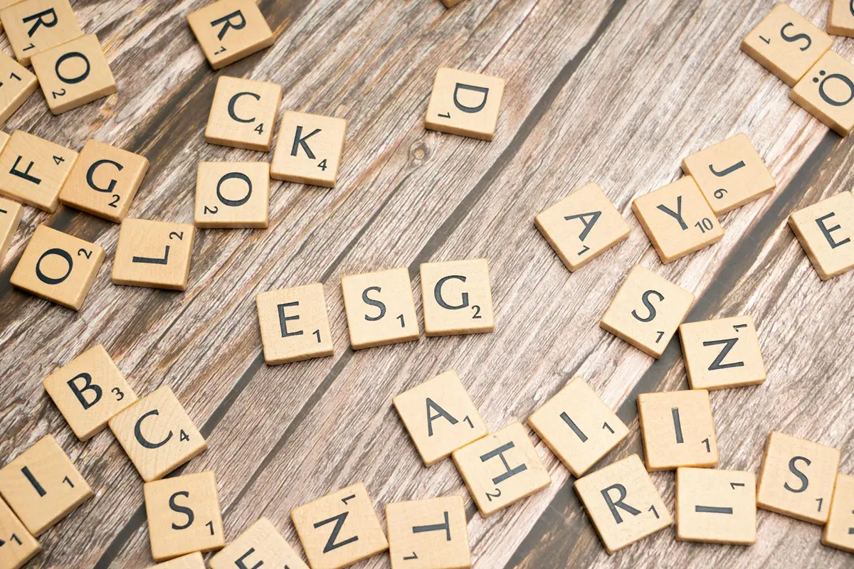 Wooden Scrabble letter tiles arranged on rustic wood background with ESG visible among scattered letters
