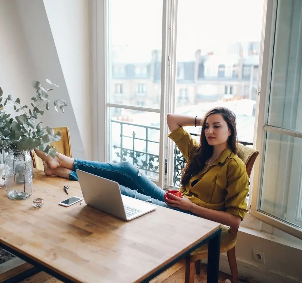 Jeune femme détendue pied sur le bureau qui réfléchit sereinement devant son ordinateur dans son salon lumineux