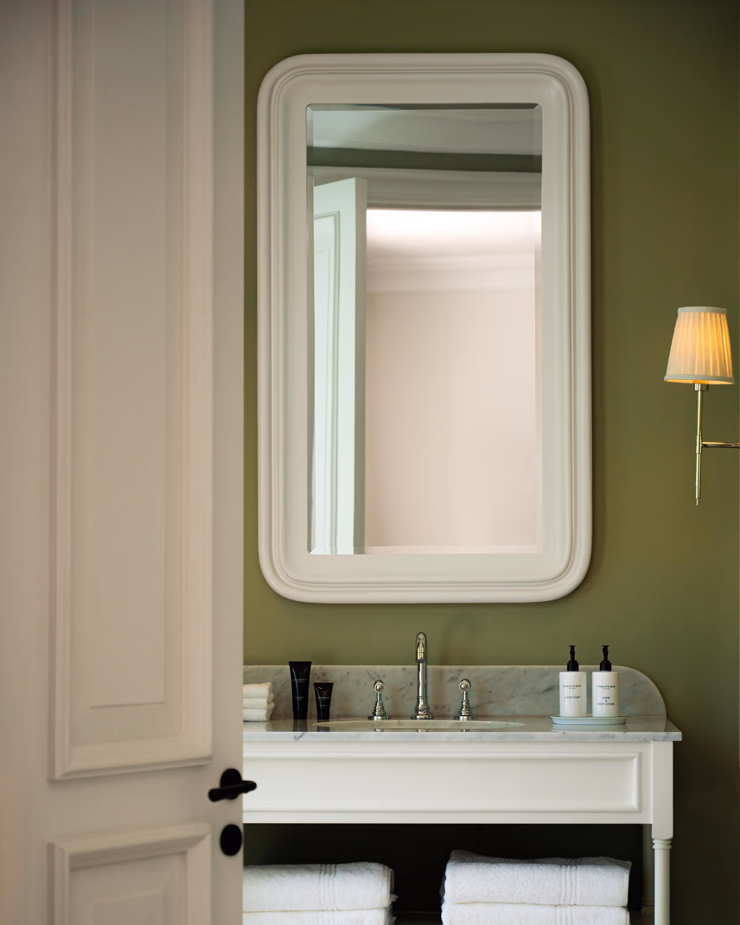 Luxury green bathroom interior with a marble sink and a beautifully framed white mirror