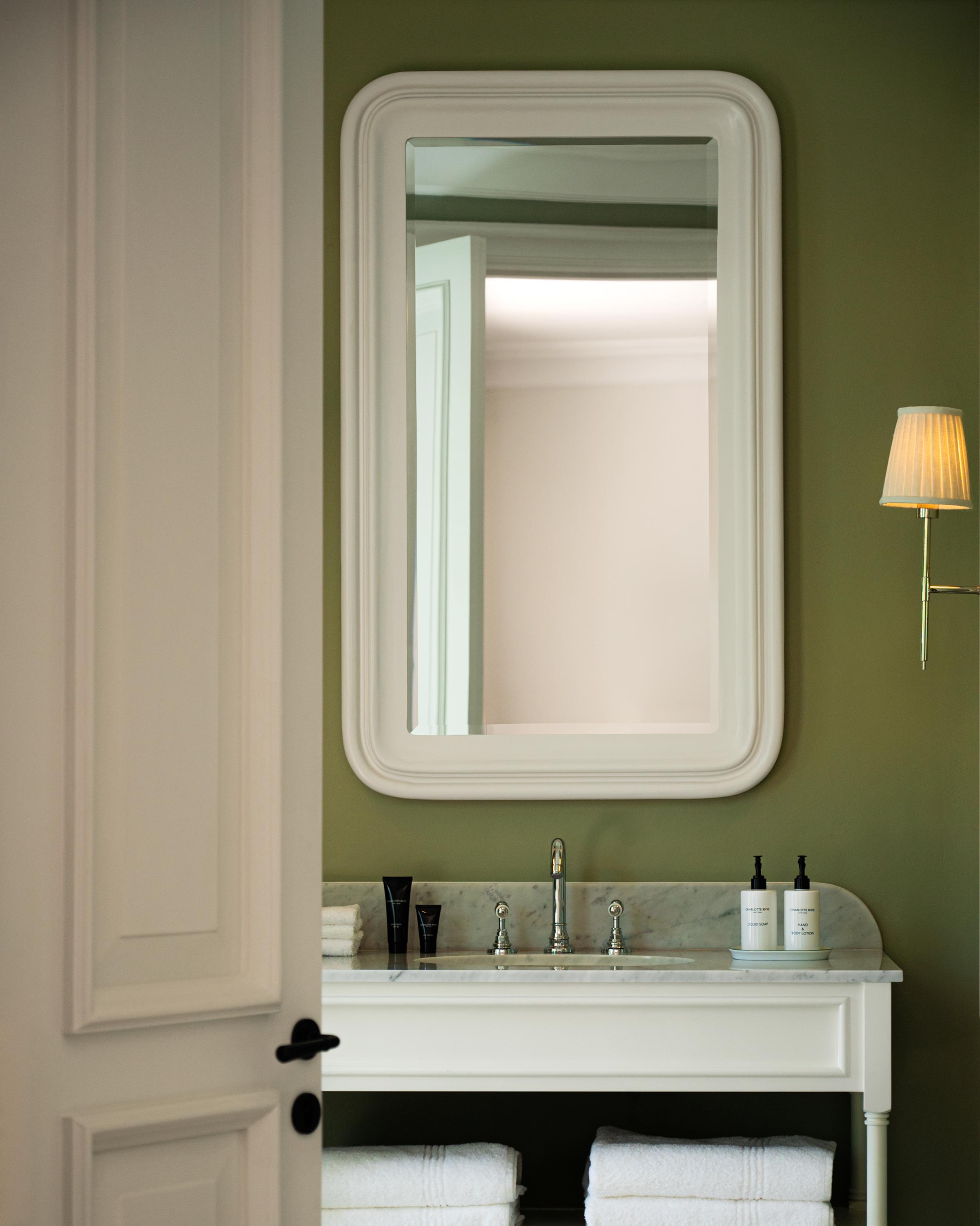 Luxury green bathroom interior with a marble sink and a beautifully framed white mirror