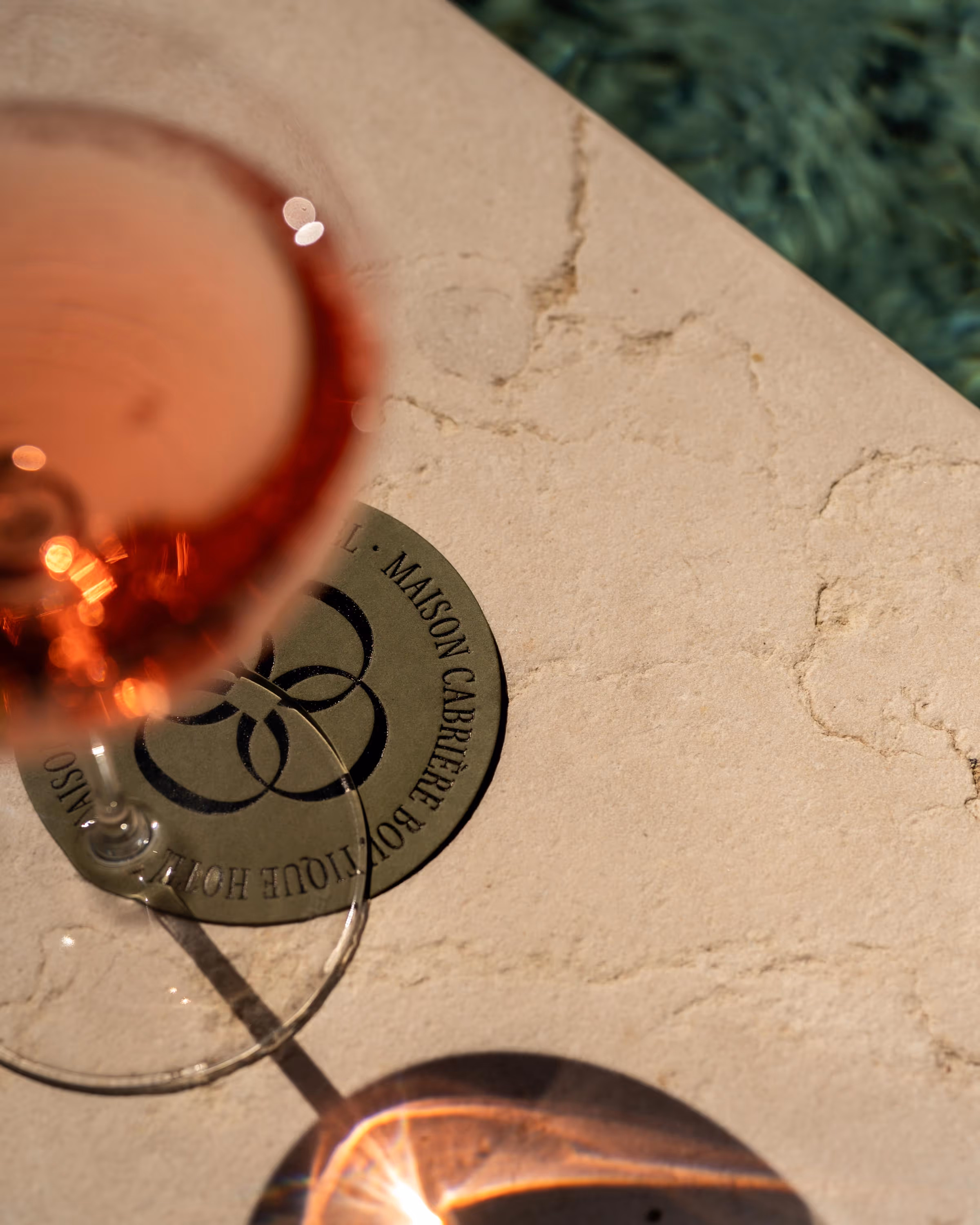 Close-up of a glass of rosé wine on a beige textured table with a circular coaster and light reflections.