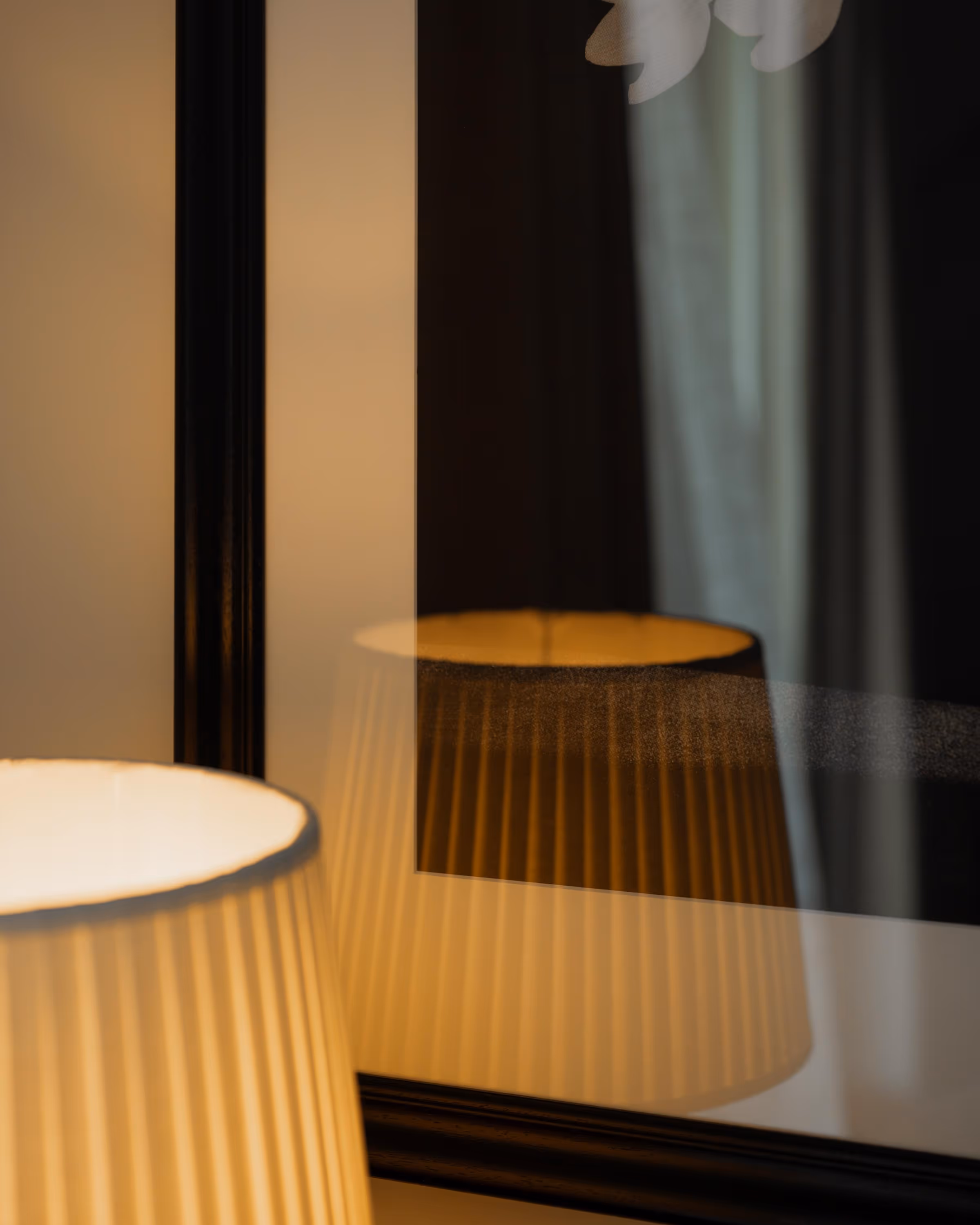 Close-up of a lit white pleated lampshade with its reflection in a black-framed mirror.