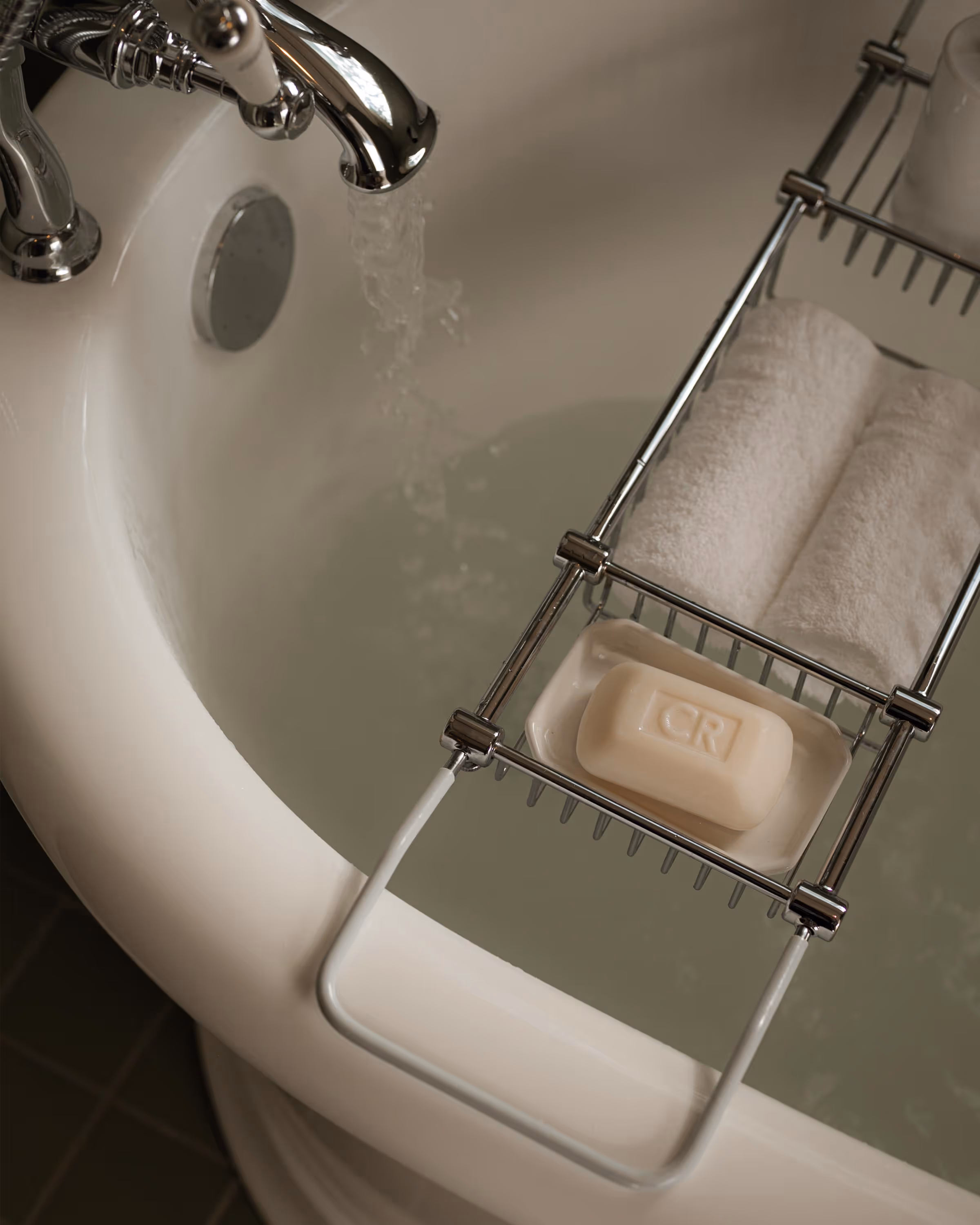 Bathtub with a chrome faucet running water and a metal bath caddy holding rolled white towels and a bar of soap.