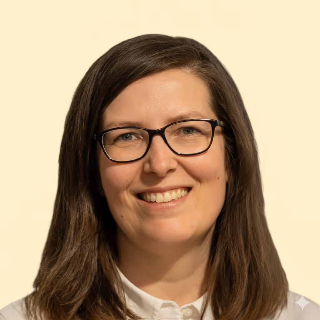 Žena se středně dlouhými hnědými vlasy, černými brýlemi a bílou košilí, která se usmívá na světlém pozadí.