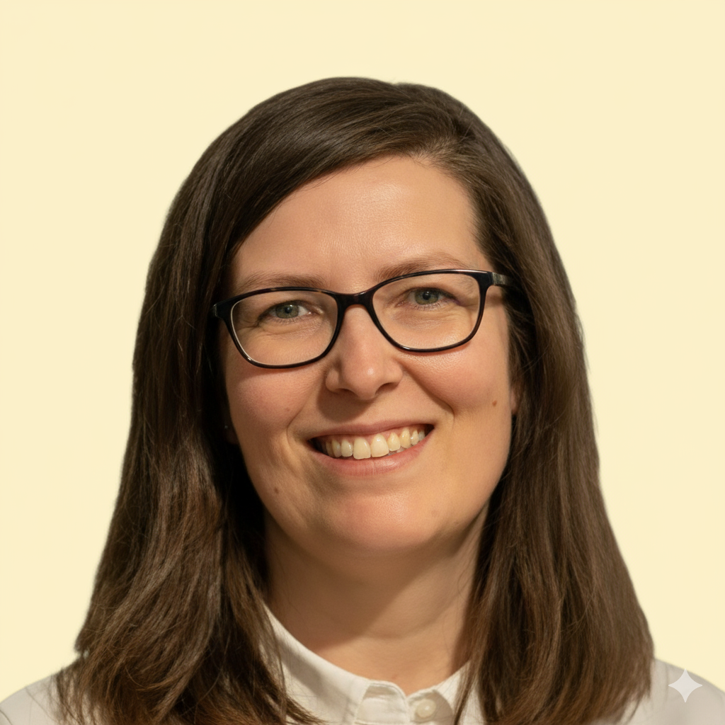 Žena se středně dlouhými hnědými vlasy, černými brýlemi a bílou košilí, která se usmívá na světlém pozadí.