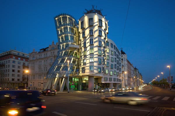 A curvy, illuminated building on the corner of a city block, silhouetted against the night sky.