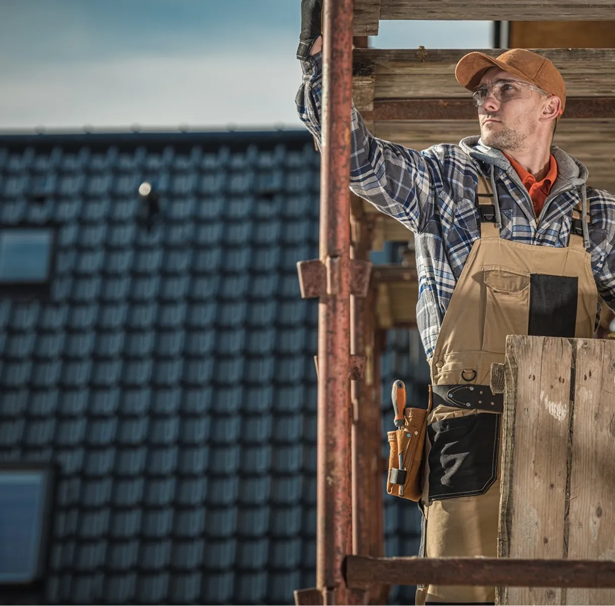 A man wearing a plaid shirt and suspenders is working on a roof.