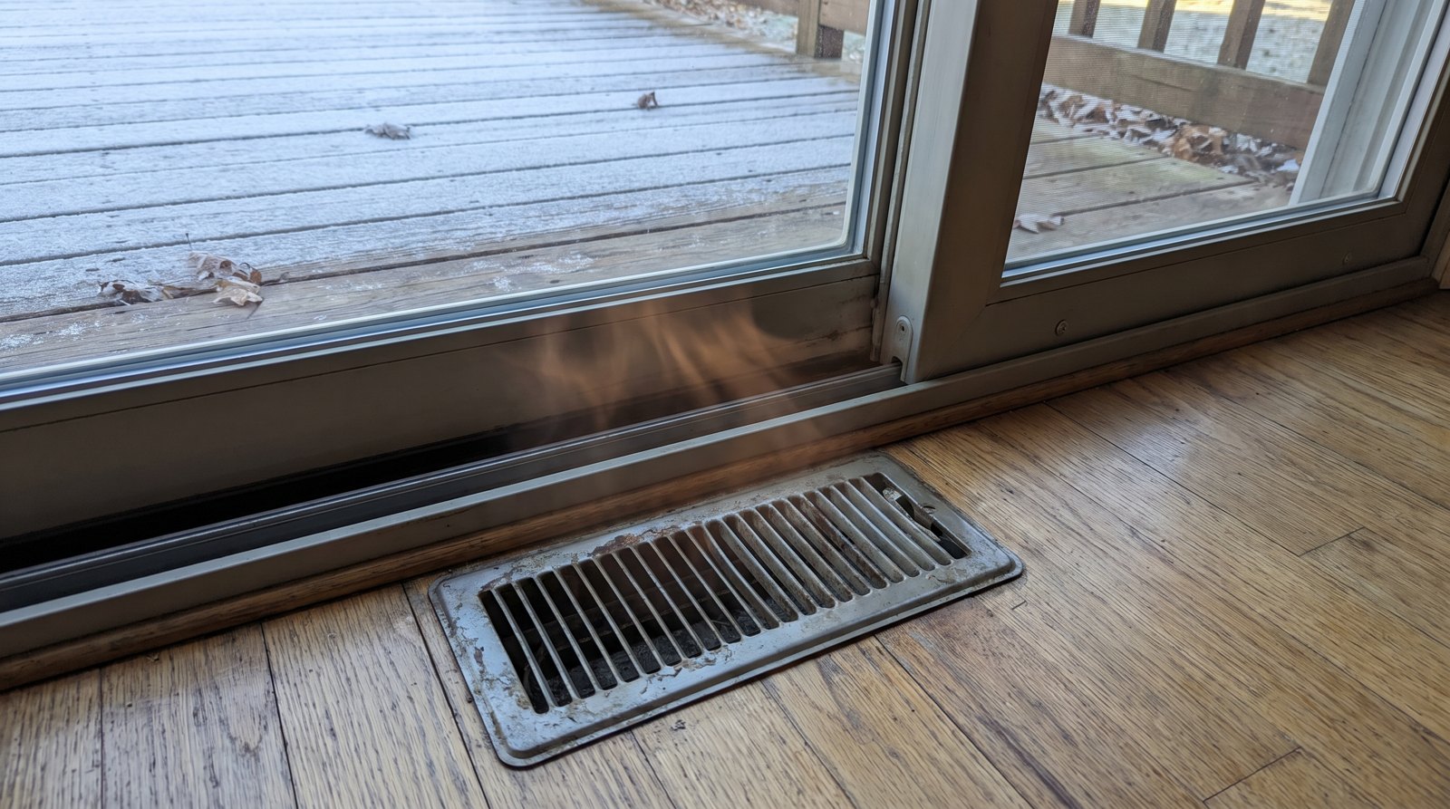 Grille de chauffage au sol installée près d'une porte patio coulissante, démontrant la synergie avec le système CVAC.
