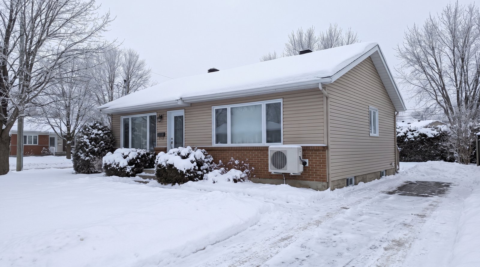Bungalow enneigé à Mascouche en hiver avec thermopompe murale installée sur le mur extérieur