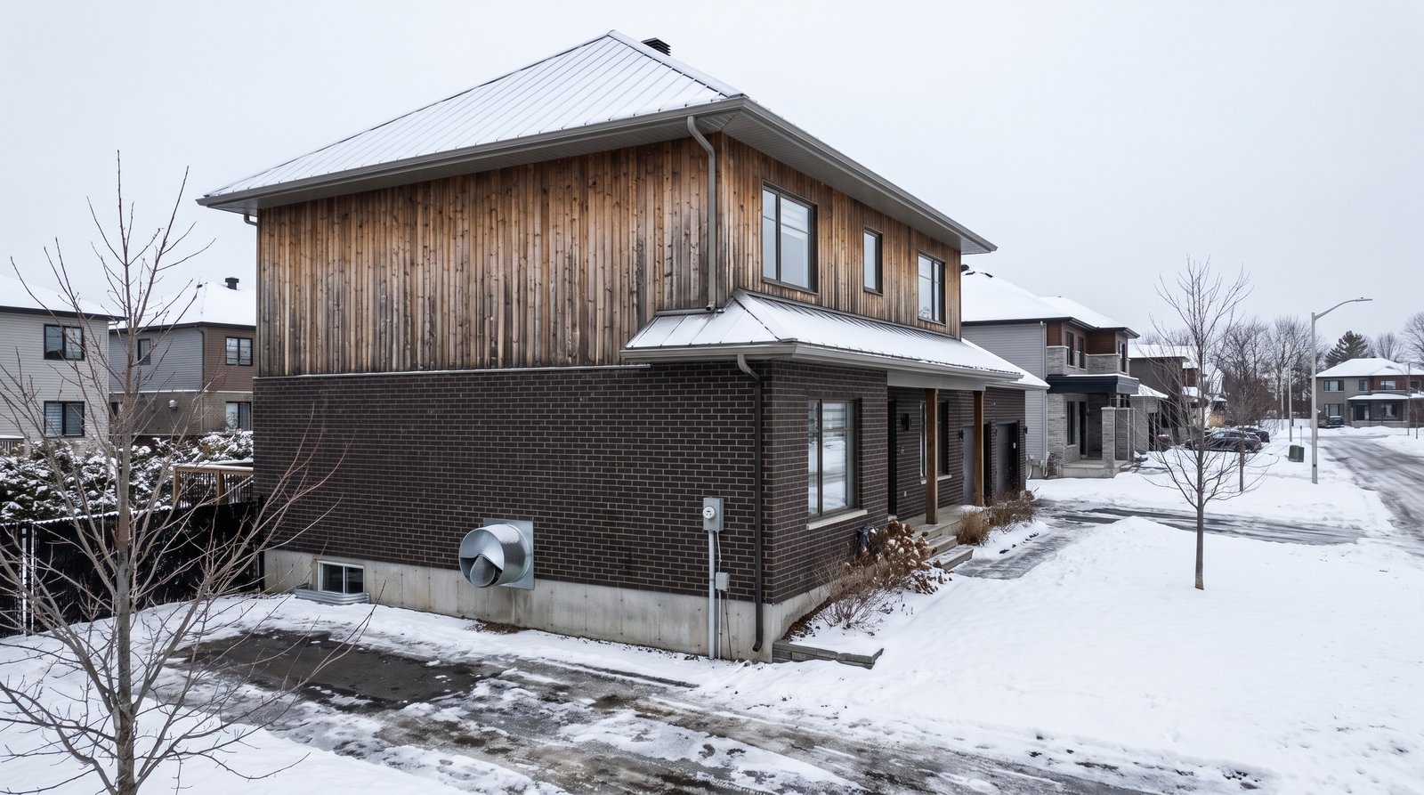 Maison résidentielle à étage à Gatineau en hiver avec une bouche d'évacuation d'échangeur d'air visible sur le mur de brique