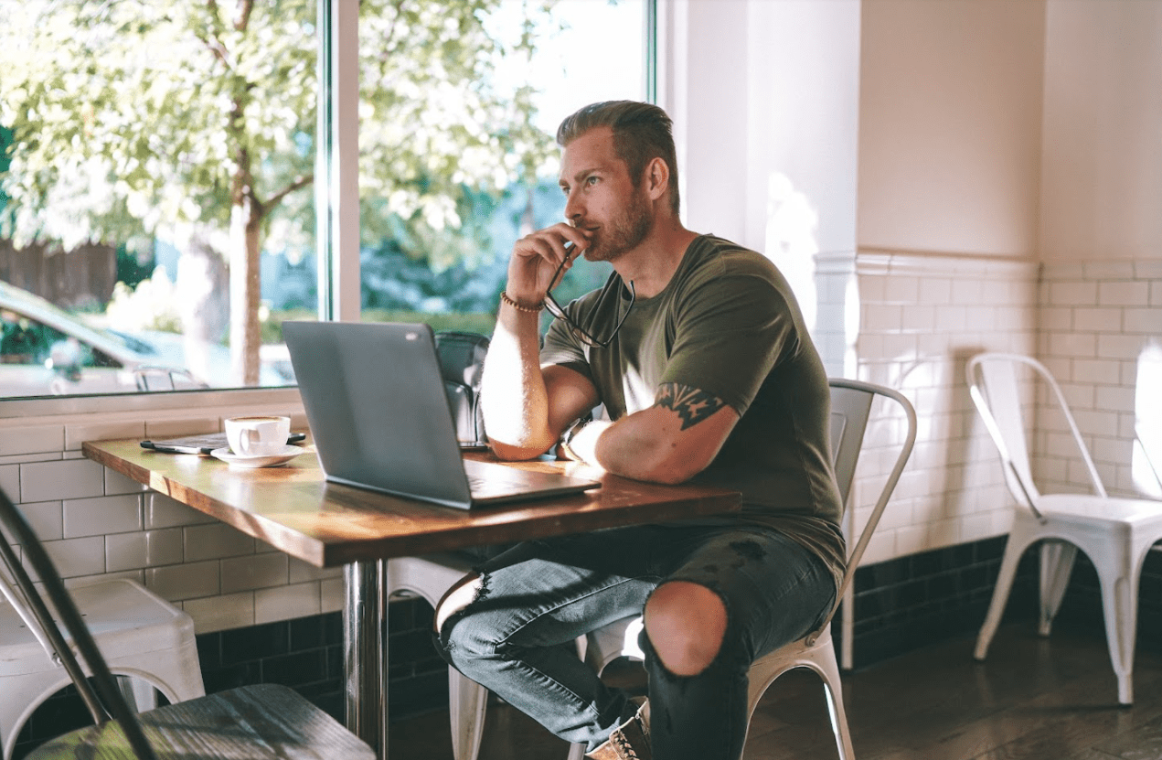 Image of Joshua Ledbetter using a laptop in a cafe staring into the distance