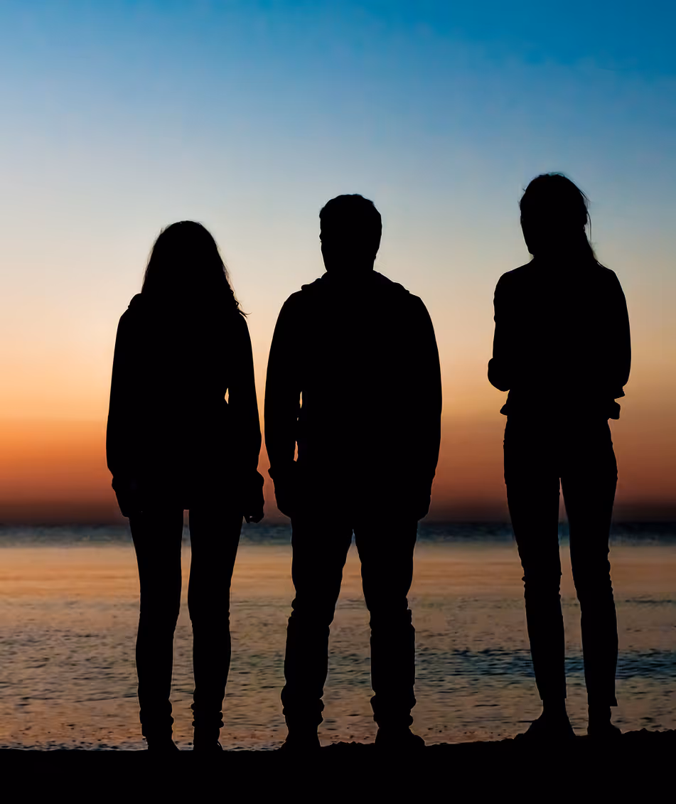 Silhouettes of three people standing on the beach looking at a sunset.