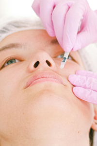 Close up of gloved hands giving a woman Filler injectables in the top of her lip at Complexion Medspa Cobourg
