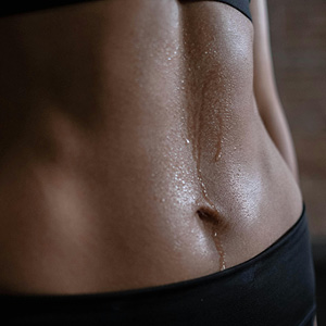 Close-up of a toned midsection with sweat dripping down the skin, wearing black workout clothing.